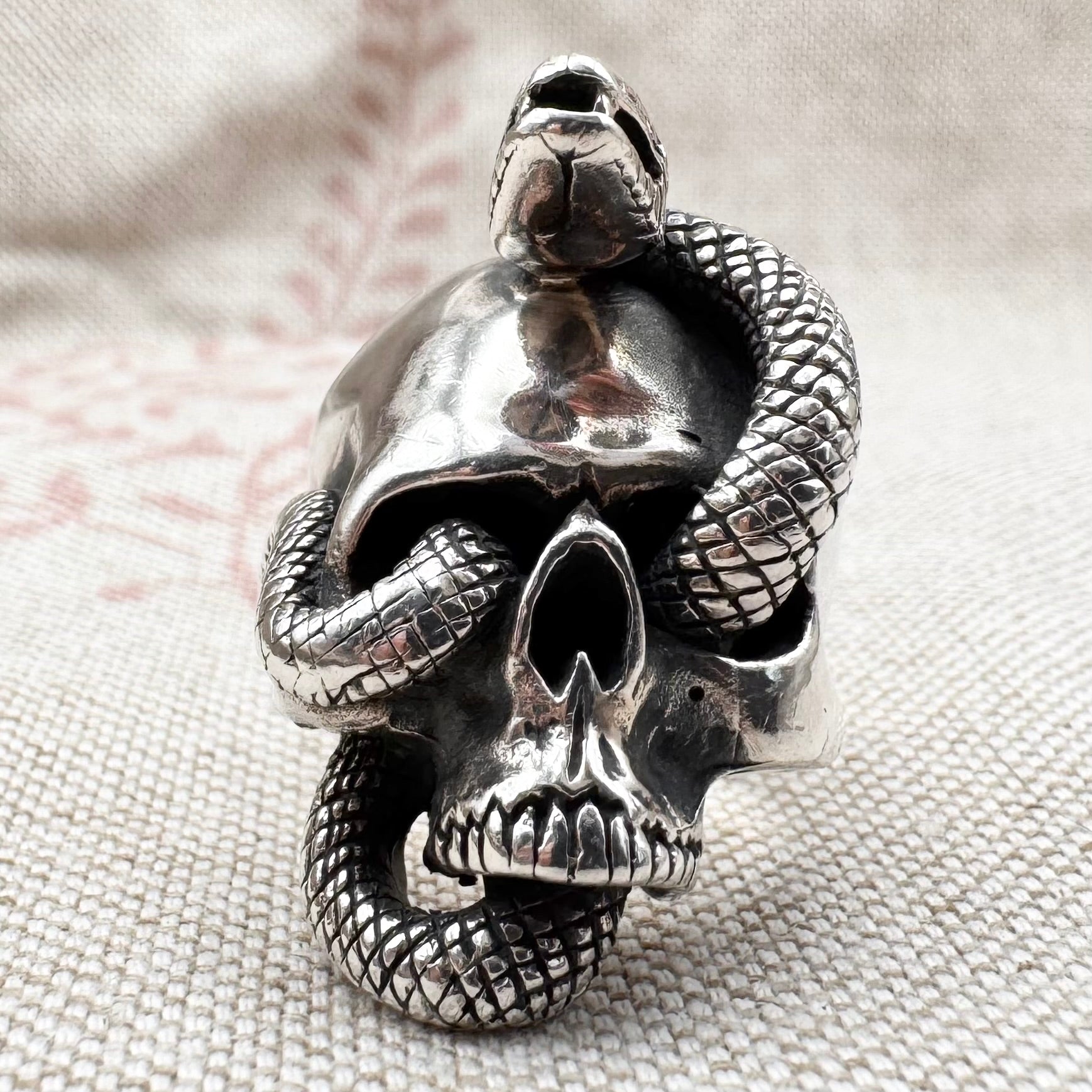 Silver skull ring with a snake wrapping around it on a textured fabric background