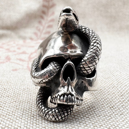Silver skull ring with a snake wrapping around it on a textured fabric background