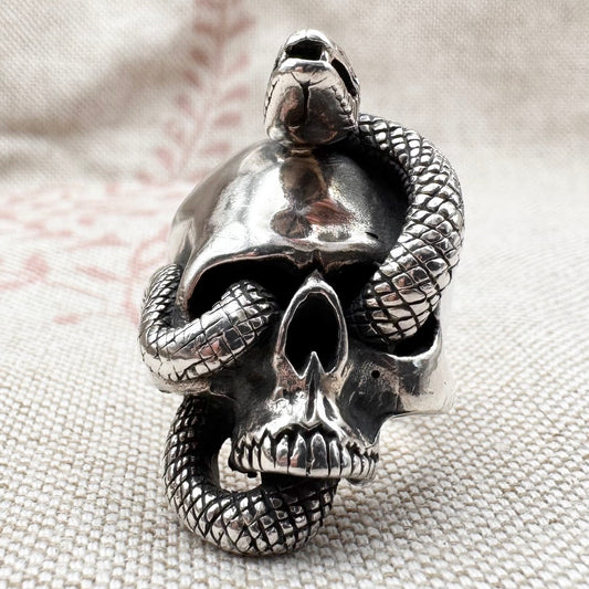 Silver skull ring with a snake wrapping around it on a textured fabric background