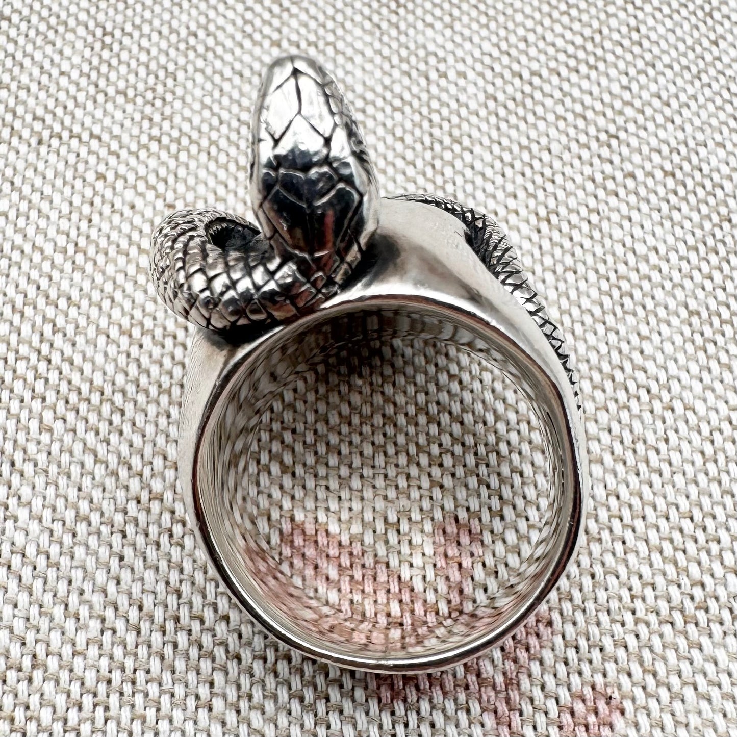 Silver ring with snake design on a textured fabric background
