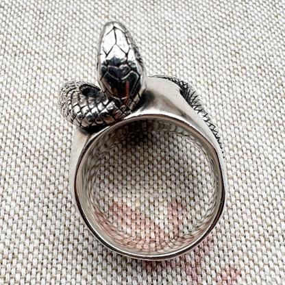 Silver ring with snake design on a textured fabric background