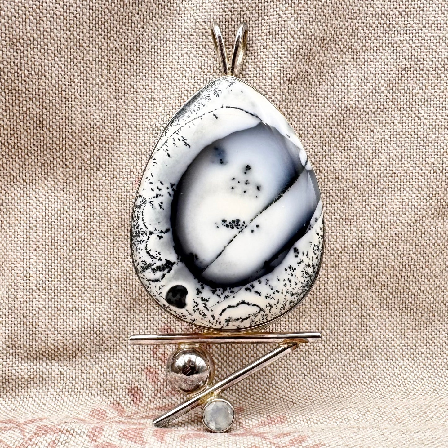 Teardrop-shaped pendant with speckled design on a beige fabric background