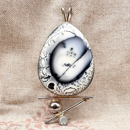 Teardrop-shaped pendant with speckled design on a beige fabric background