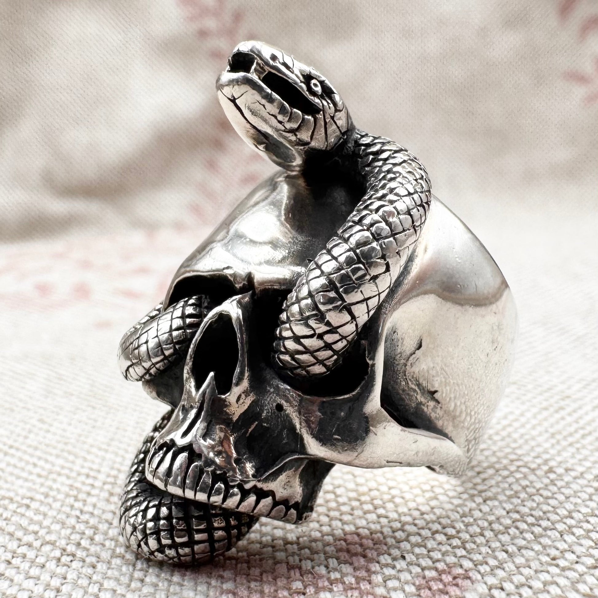 Silver skull ring with a snake coiled around it on a textured fabric background