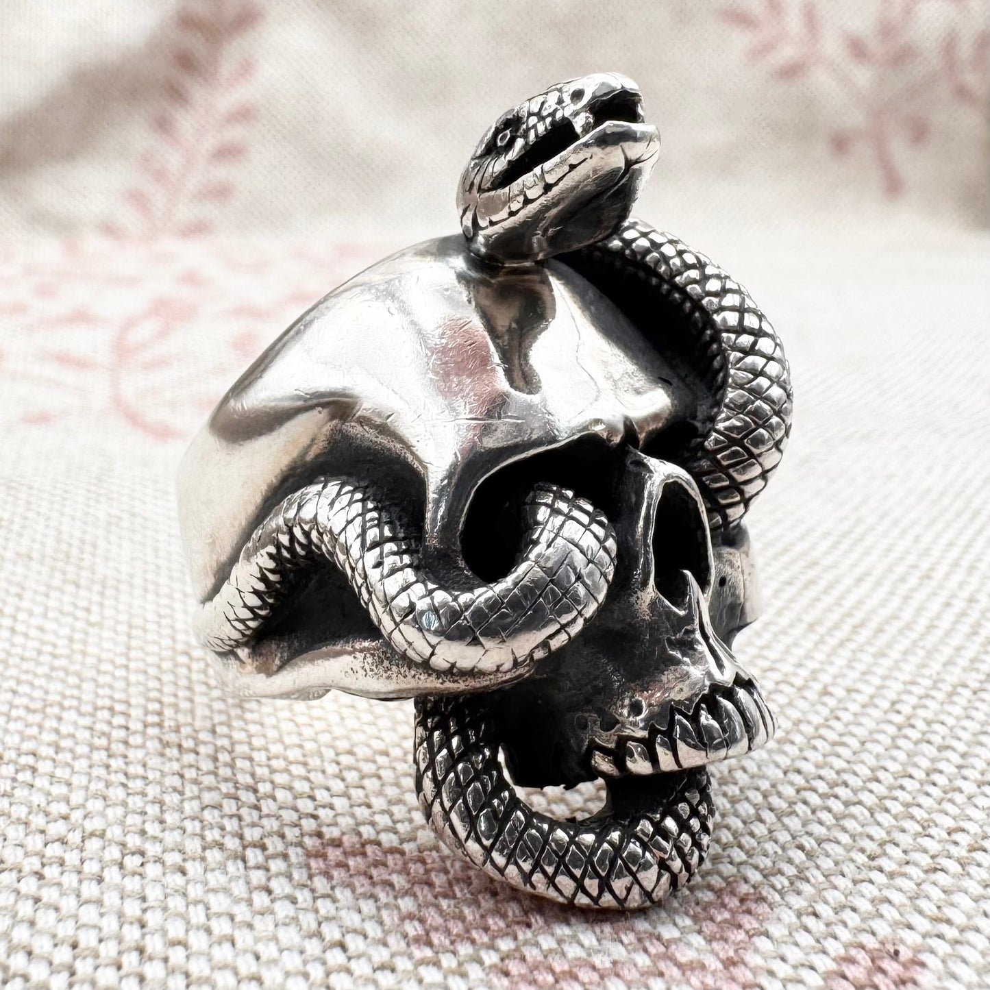 Silver skull ring with a snake coiled around it on a textured fabric background