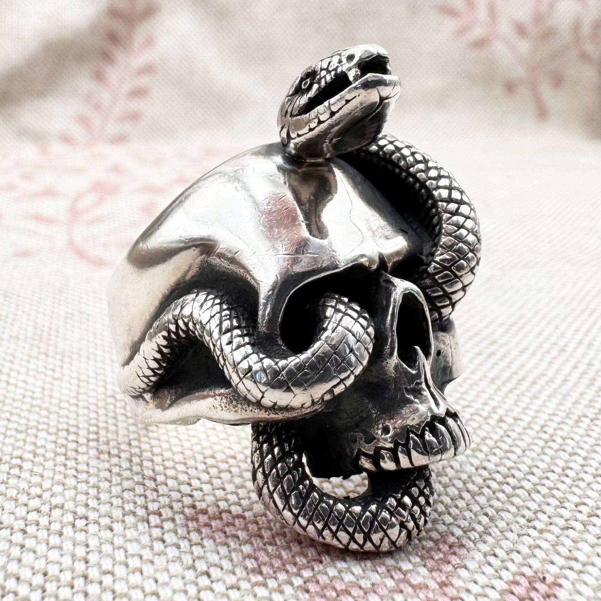 Silver skull ring with a snake coiled around it on a textured fabric background