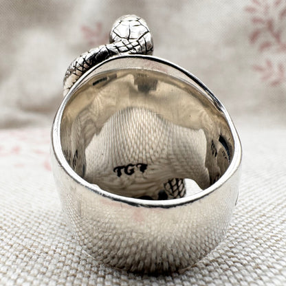 Close-up of a silver ring with textured surface and engraved text on a textured fabric background